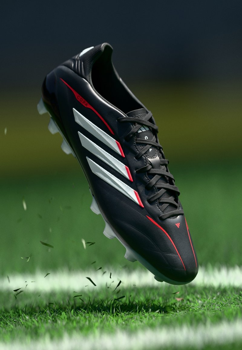 Zwarte voetbalvoetbalschoen met witte strepen en rode accenten, met een gestructureerd oppervlak en een lichtgewicht ontwerp, zwevend boven het gras.