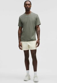 Olivegrøn t-shirt med rund hals, kombineret med lyse beige shorts. Modellen har hvide sportssko og ankelsokker på.