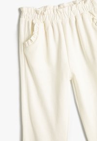 Crème kleurige sweatpants met een elastische tailleband, rimpelige zakranden en een zachte, gladde textuur. Bevat één zijzak.