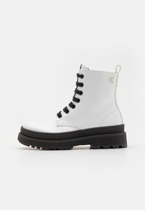 Botte de cheville en cuir verni blanc avec des lacets noirs, semelle épaisse noire et un petit talon. Présente un accent logo à l'arrière.