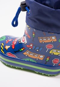 Botte imperméable pour enfants avec une base bleue, ornée de motifs colorés sur le thème de la circulation. Semelle verte et cordon bleu en haut.