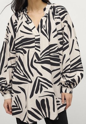 Blusa de corte amplio con estampado geométrico abstracto negro sobre tejido beige claro, con mangas largas abullonadas y escote en V con una tapeta frontal parcial.