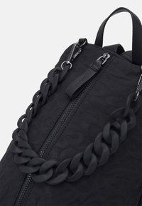 Svart ryggsäck med en texturerad yta, ett flätat kedjehandtag och ett ficka med dragkedja, försett med stilren svart metall och detaljer.