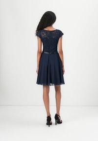 Navy dress with lace bodice, cap sleeves, and a flared skirt. Features a satin waistband and seamless back design. Worn with black heels.