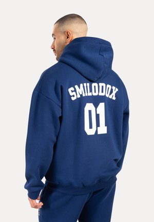 Sudadera azul marino de tejido suave con un gran logo blanco de "SMILODOX" y "01" en la parte posterior, con capucha ajustable y puños de canalé.