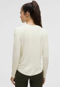 Pikkade varrukatega heledast kreemjast särgist ümmarguse kaelusega, tekstuurse kangaga ja kerge kõrge-kõrge hemiga, kantud koos tihedalt istuvate tumeroheliste pükstega.