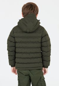 Grön puffjacka med horisontellt quiltat mönster, huva och elastiska ärmar. Bärs över matchande gröna cargobyxor.