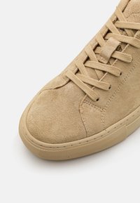 Beige kevlar-kenkät, joissa on pyöreä kärki, tekstuuripinta ja litteät nauhat. Ominaisuuksiin kuuluu kumipohja, jossa on huomaamaton kuvio ja ompeluyksityiskohtia.