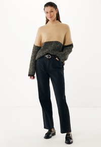 Jersey de punto a cuadros en beige y negro con un cuello alto y mangas sueltas, combinado con pantalones negros de cintura alta y zapatos brillantes.