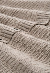 Beige knitted fabric with ribbed cuffs, textured stitch patterns, and soft folds creating a cozy appearance.