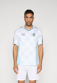 Lichtblauw voetbalshirt met een geruit patroon, zwarte accenten, kraag en Champion-logo. Draagt samen met witte shorts. Korte mouwen.