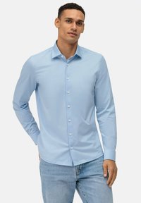 Hellblaues langärmliges Hemd mit Knopfverschluss und standardmäßigem Kragen, glatter Textur und weißen Knöpfen, kombiniert mit hellblauen Jeans.