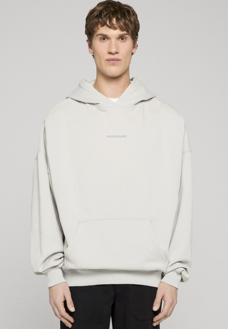 Světlé šedé mikina s kapucí, přední kapsou a žebrovanými manžetami. Na hrudi je decentní potisk s logem "PEGADOR". Měkká textura látky.