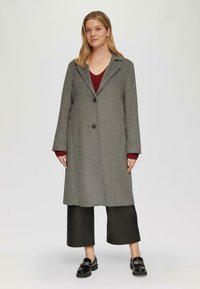Grijze wollen mix jas met een notch-kraag, twee knopen en zijzakken, gecombineerd met een bordeauxkleurig top en brede zwarte broek.