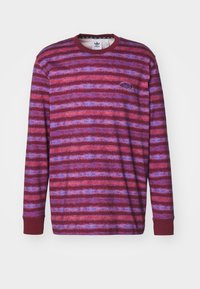 Hosszú ujjú, crewneck póló, piros, lila és kék árnyalatú, texturált csíkozással. Rugalmas mandzsettákkal és egy kis logóval a mellkason.