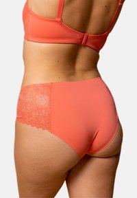 Sous-vêtements corail en tissu lisse avec des accents en dentelle sur les hanches, présentant une taille mi-haute et un design sans coutures.