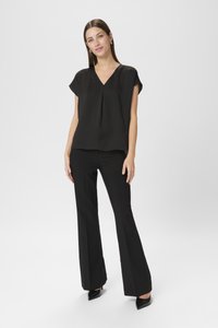 Sort kortærmet blouse med V-hals og plisseret detalje, parret med sorte brede bukser og spidse hæle. Glat tekstur.
