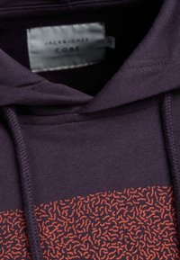 Sudadera navy con un patrón texturizado en naranja en la mitad inferior, que cuenta con una capucha con cordones y una etiqueta interna con información de la marca.