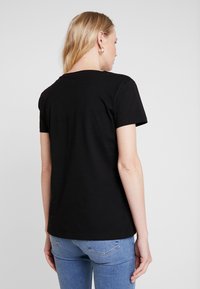 Schwarzes Baumwoll-T-Shirt mit kurzen Ärmeln, Rundhalsausschnitt und glatter Textur, das von hinten auf einer Person dargestellt wird.
