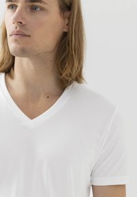 Bílý bavlněný tričko s výstřihem do V a krátkým rukávem, hladká textura a přiléhavý střih, zobrazené na jednobarevném pozadí.