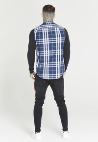 Long-sleeve shirt with a blue and white plaid back, black fitted sleeves, and black pants, featuring a tag on the waistband.