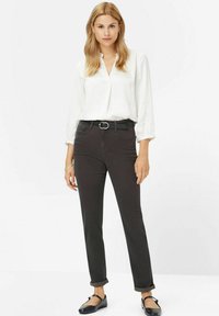 Schwarze Slim-Fit-Jeans mit mittelhohem Bund, ausgestattet mit umgeschlagenen Säumen, vorderen Taschen und einem strukturierten schwarzen Gürtel mit einer silbernen Schnalle.