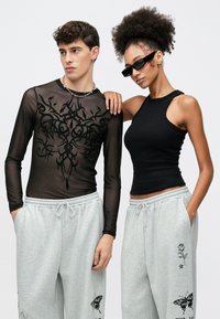 Mustast pikast varrukast võrgusärk rikkaliku mustriga, hallid dressipüksid liblikate ja rooside trükistega ning tähelepanelikult istuv must top.