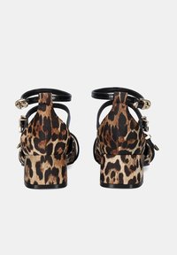 Sandalias de tacón alto de estampado de leopardo con una correa negra, tejido texturizado y tacón cuadrado. Presentan acentos de hardware dorado en las correas.