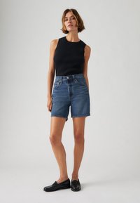 Blå denimshorts med hög midja, fransad fåll och femfickorsdesign. Kombinerat med en svart ribbad ärmlös topp och svarta loafers.