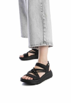 Sandalias negras con tiras, con una suela gruesa y texturizada y tiras que se superponen. Diseño de punta abierta, con una correa trasera segura y un detalle de hardware minimalista.