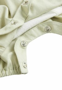 Tessuto verde chiaro con una morbida texture, caratterizzato da bottoni a pressione in metallo e orlo arricciato. Il tessuto presenta una leggera elasticità e stratificazione.