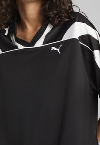 Maillot de sport noir avec des rayures horizontales blanches, un col et un petit logo Puma à l'avant. Fabriqué en matériau texturé et respirant.