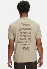 Beige katoenen t-shirt met grote bruine tekst: "Under Armour" en verschillende termen voor "sport" in meerdere talen, naast een wereldkaart grafiek.