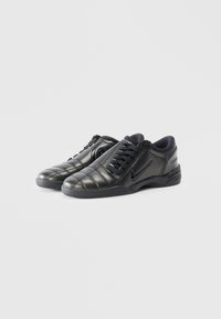 Black athletic shoes with a smooth, glossy finish, featuring a quilted design, lace-up closure, and a prominent Nike logo on the side.