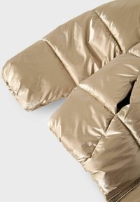 Sezione di giacca a vento in metallo dorato con design trapuntato. Texture liscia e lucida con polsini elasticizzati e dettagli delle cuciture visibili.