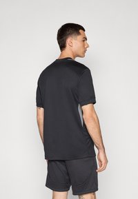 Zwart sportt-shirt met korte mouwen en een ronde hals. Het materiaal is lichtgewicht en gestructureerd, met grijze accenten aan de zijkanten.