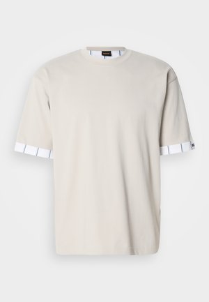 T-shirt di cotone beige con scollo a girocollo. Maniche corte con un dettaglio a righe bianche agli orli. Design semplice e casual.