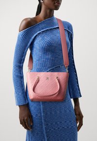 Pink patterned handbag with a textured finish and gold hardware, worn with a blue ribbed dress featuring an off-shoulder design and button accents.