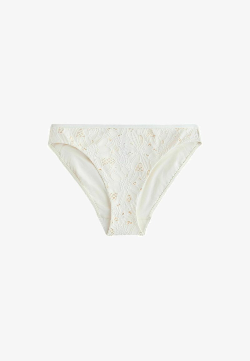 Bas de bikini blanc avec superposition de dentelle florale et motif partiellement transparent, présenté à plat sur un fond blanc.