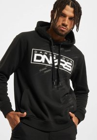 Sudadera negra con bolsillo frontal tipo canguro y capucha con cordón. Presenta un texto en negrita blanco "DANGEROUS" y un patrón repetido en un gris sutil.