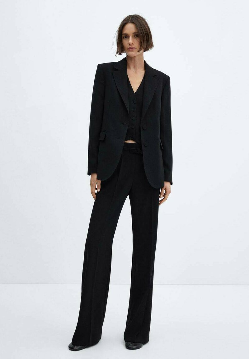 Schwarzer Anzug mit einem taillierten Blazer mit Reverskragen, einer schmalen Weste mit Knöpfen und einer weit geschnittenen Hose. Glatte Textur und minimales Design.