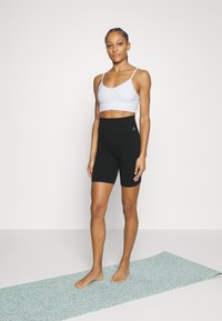 Pantalones cortos de ciclismo de talle alto en negro y un sujetador deportivo corto blanco. La esterilla de yoga debajo es de color verde menta con una superficie texturizada.
