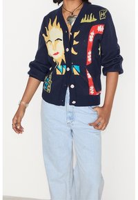 Mörkblå cardigan med en färgglad sol och abstrakta mönster, tillverkad av stickat tyg med knappar fram och ribbade ärmslut.