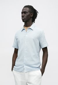 Overhemd met korte mouwen en knopen in lichtblauw met een geruit patroon. Gemaakt van zachte stof, met een spitse kraag en een lichte textuur.
