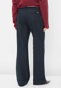 Marineblauwe broek met streepjes en een brede pijp. De stof is glad met een subtiele glans. Voorzien van achterzakken en een omgeslagen zoom.