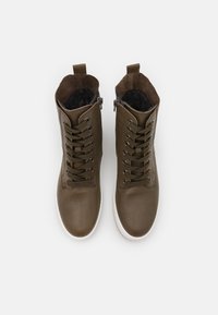 Bottes chevilles en cuir brun avec lacets, une fermeture éclair sur le côté et une semelle en caoutchouc blanc. L'intérieur comporte un revêtement textile noir.