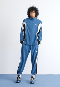 Track jacket and pants set in blue, featuring black and white accents. Smooth fabric, zip-up design, with logo on the chest.