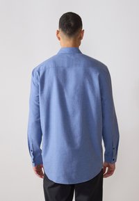 Chemise à manches longues bleue en tissu texturé, avec un col et des poignets à boutons, ourlet incurvé, et un dos droit.