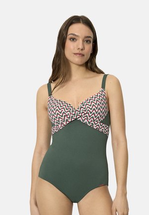 Mujer con traje de baño de una pieza verde, con el busto estampado y la parte inferior lisa, posando contra un fondo claro y sencillo.