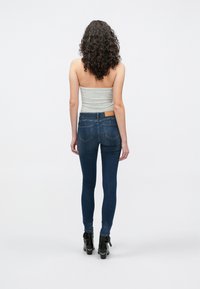 Στενά τζιν σε σκούρο μπλε ντένιμ με λεία υφή, που διαθέτουν πίσω τσέπες και καφέ δερμάτινο ταμπελάκι στη μέση. Μοντέλο που φοράει μαύρα τακούνια.